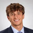 Studio headshot of Maclane Zich in a navy suit and striped tie